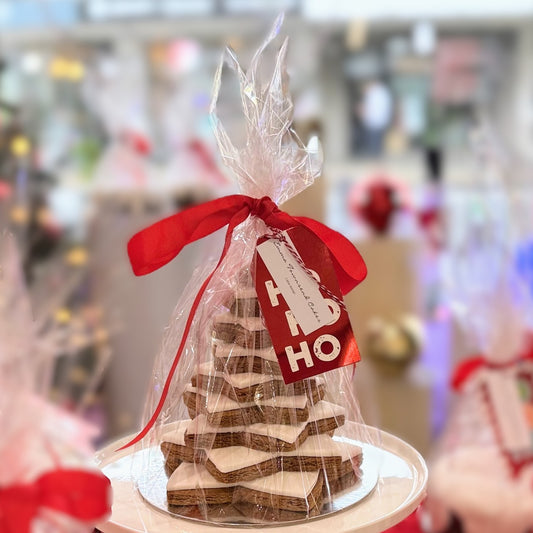 A gingerbread star tree dessert presented on a plate, wrapped in cellophane with a red ribbon, and placed on a counter.