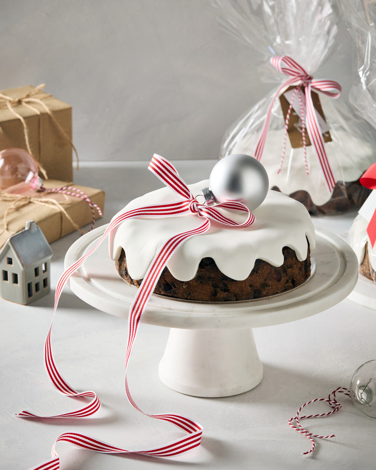 Christmas fruit cake with white fondant icing, a red and white striped ribbon and a silver bauble on a white cake stand