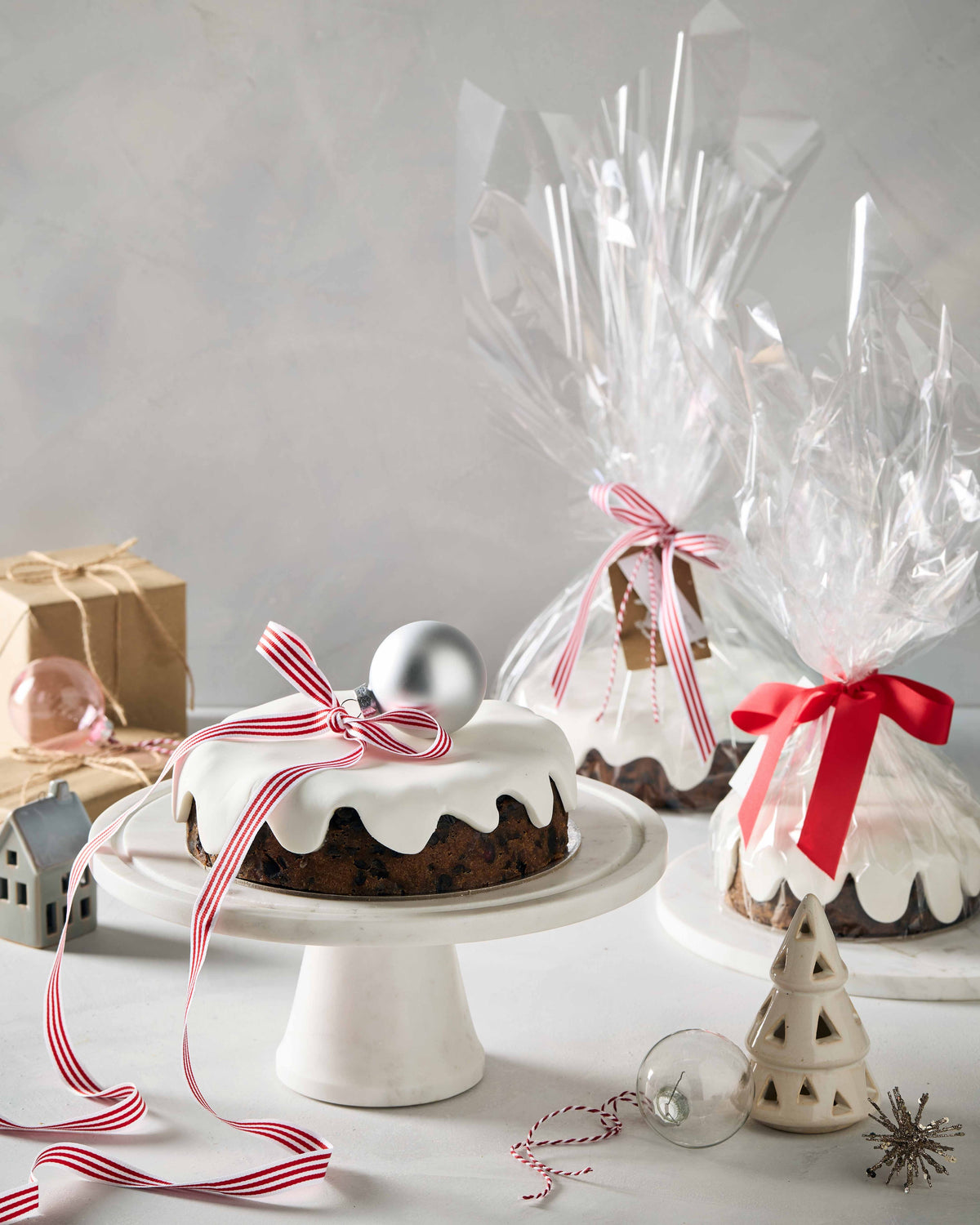 Christmas cake on a stand beside two Christmas cakes gift wrapped in cellophane with ribbon and tags