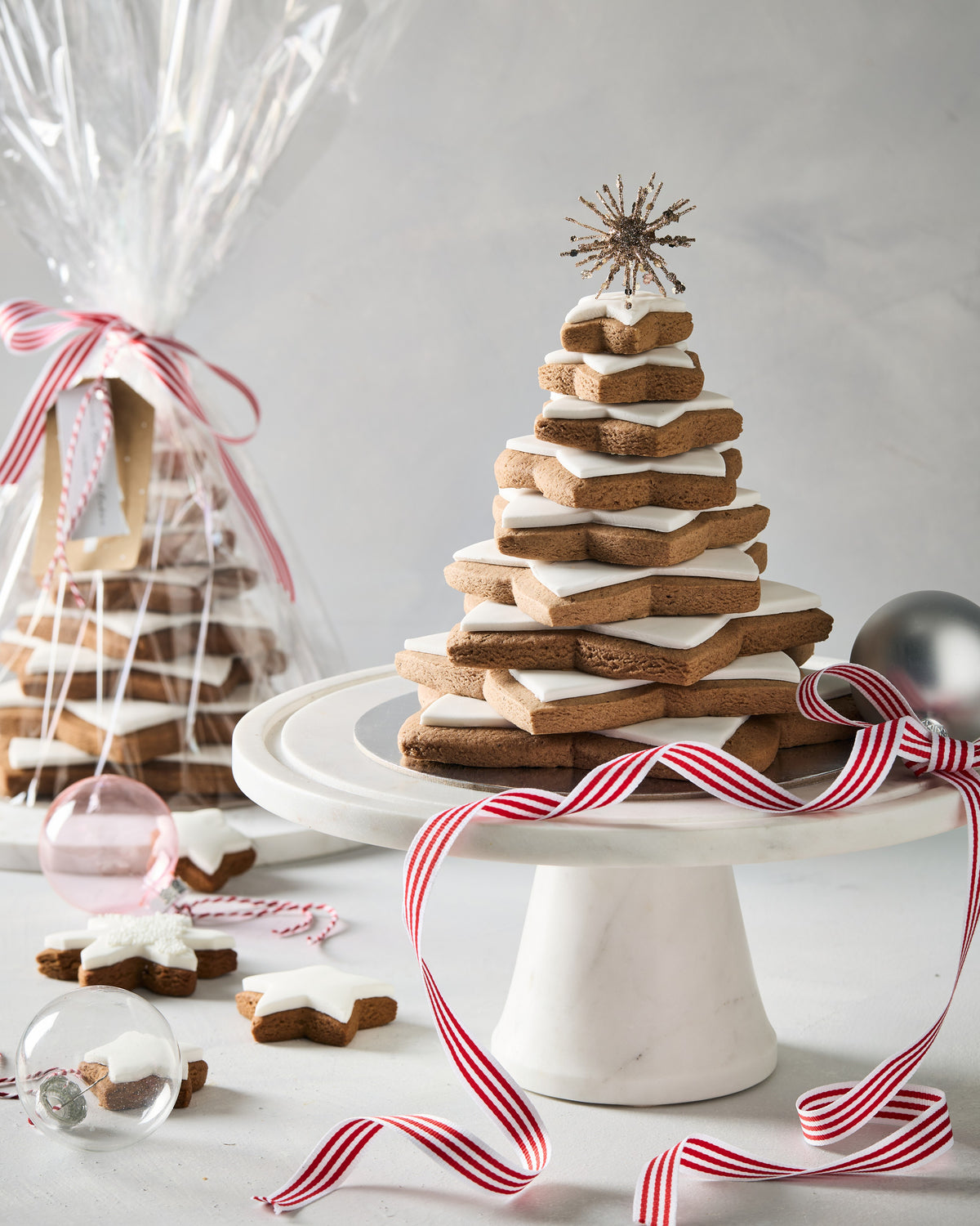 Gingerbread star tree of stacked iced star cookies on a white cake stand, with a gift wrapped star tree behind